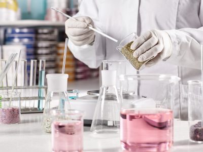 Biotechnology and pharmacology concept. Laboratory young clever worker standing near table surrounded with glass beakers filled with colorful liquid working at discovering new kind of vegetation.